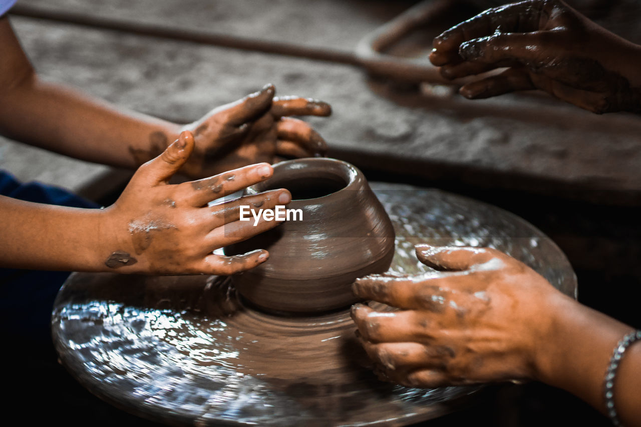 Cropped hands of people making pot in workshop
