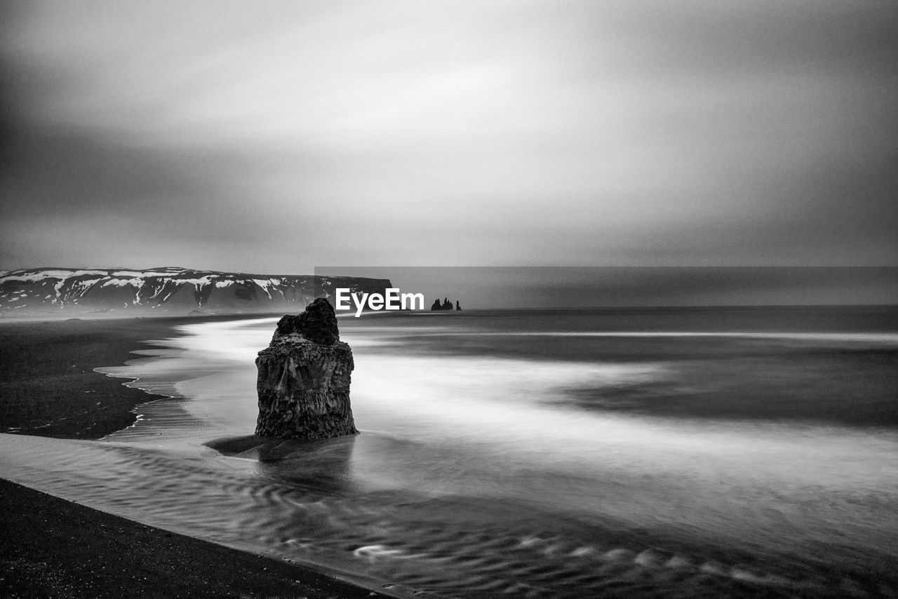 Scenic view of sea and mountain against cloudy sky during winter