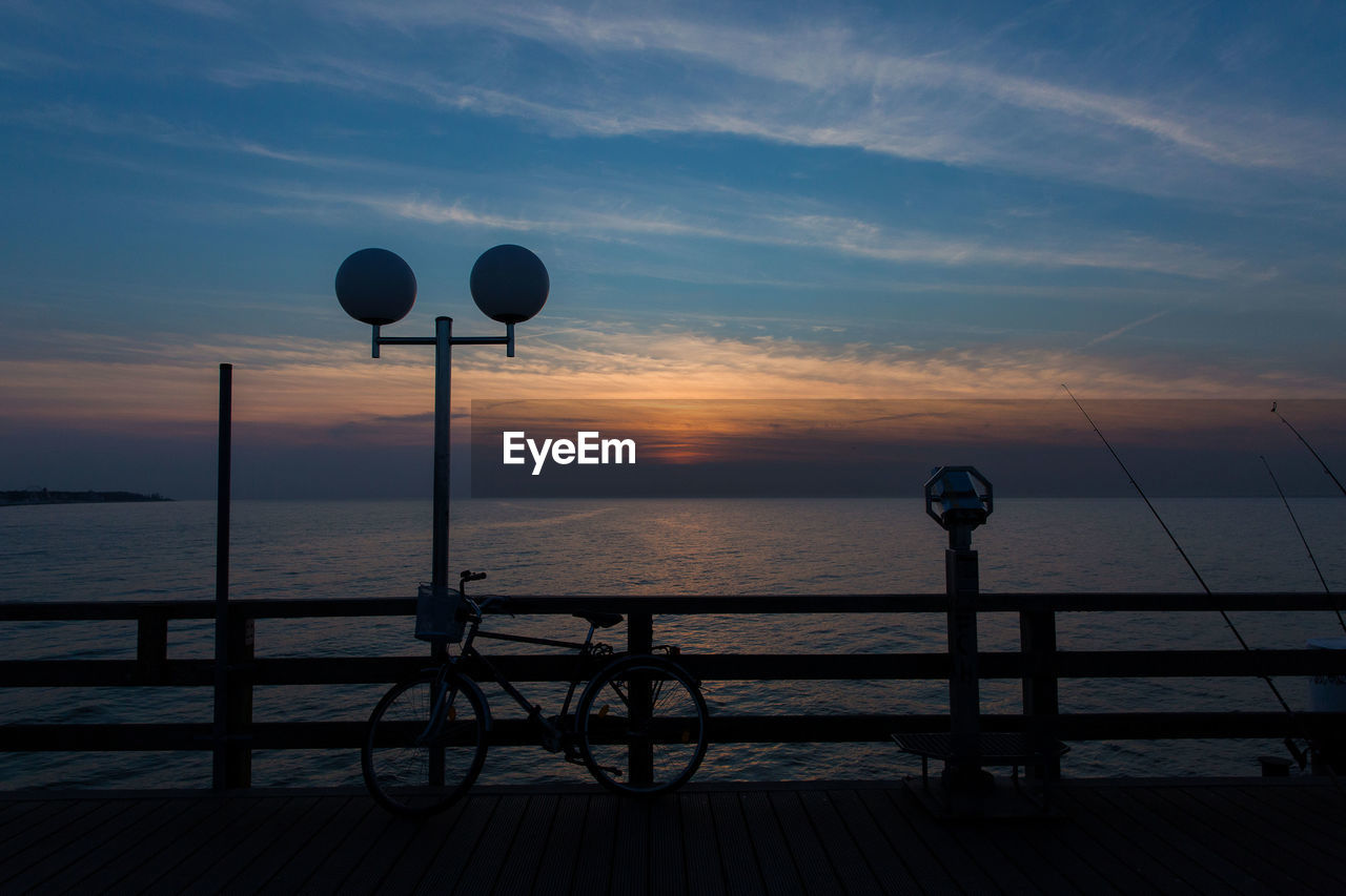 Bicycle parked on pier against sea during sunset