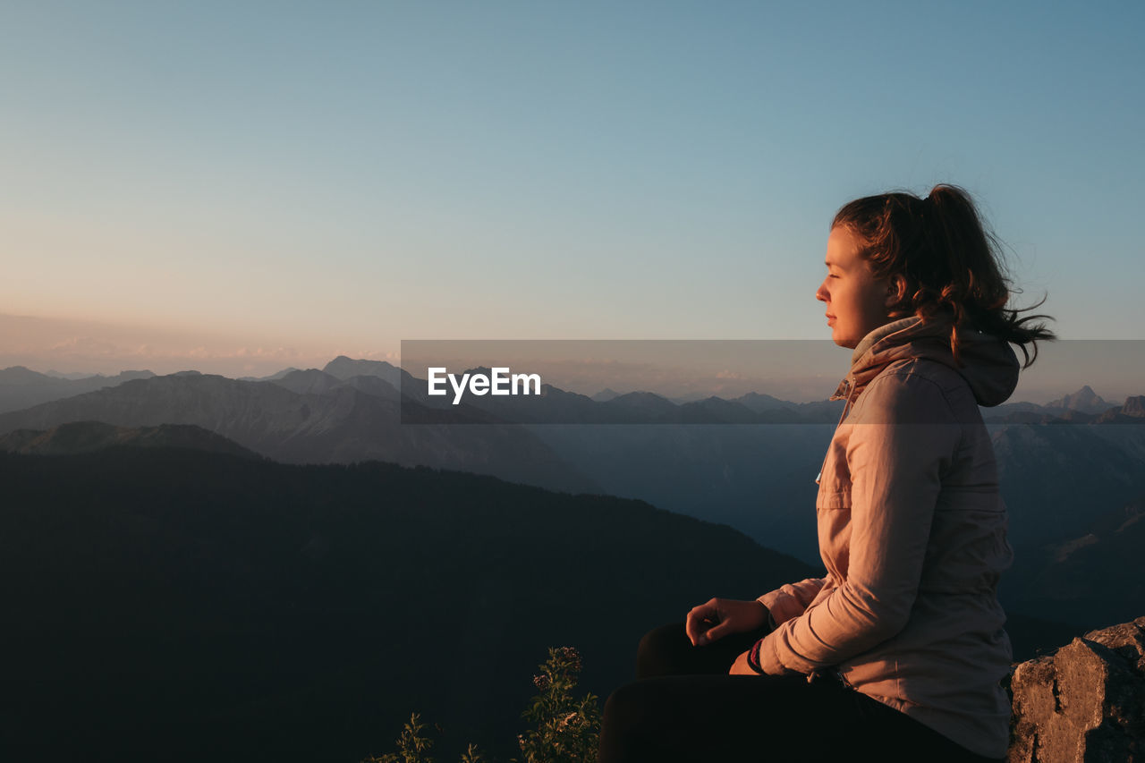 Woman sitting on mountain against sky during sunrise 