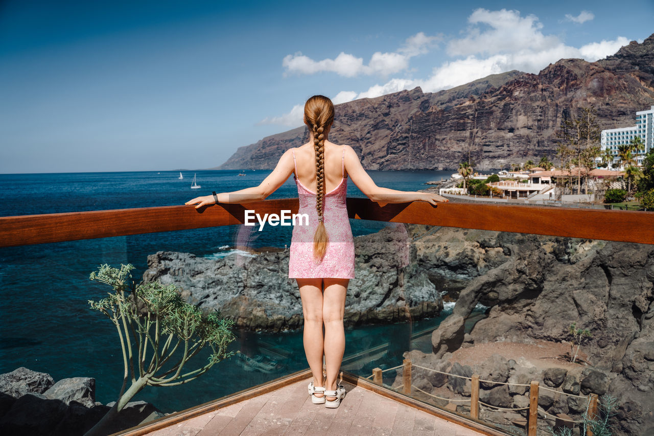 Long haired woman enjoys landscape of los gigantes cliffs and blue ocean in tenerife, canary island.