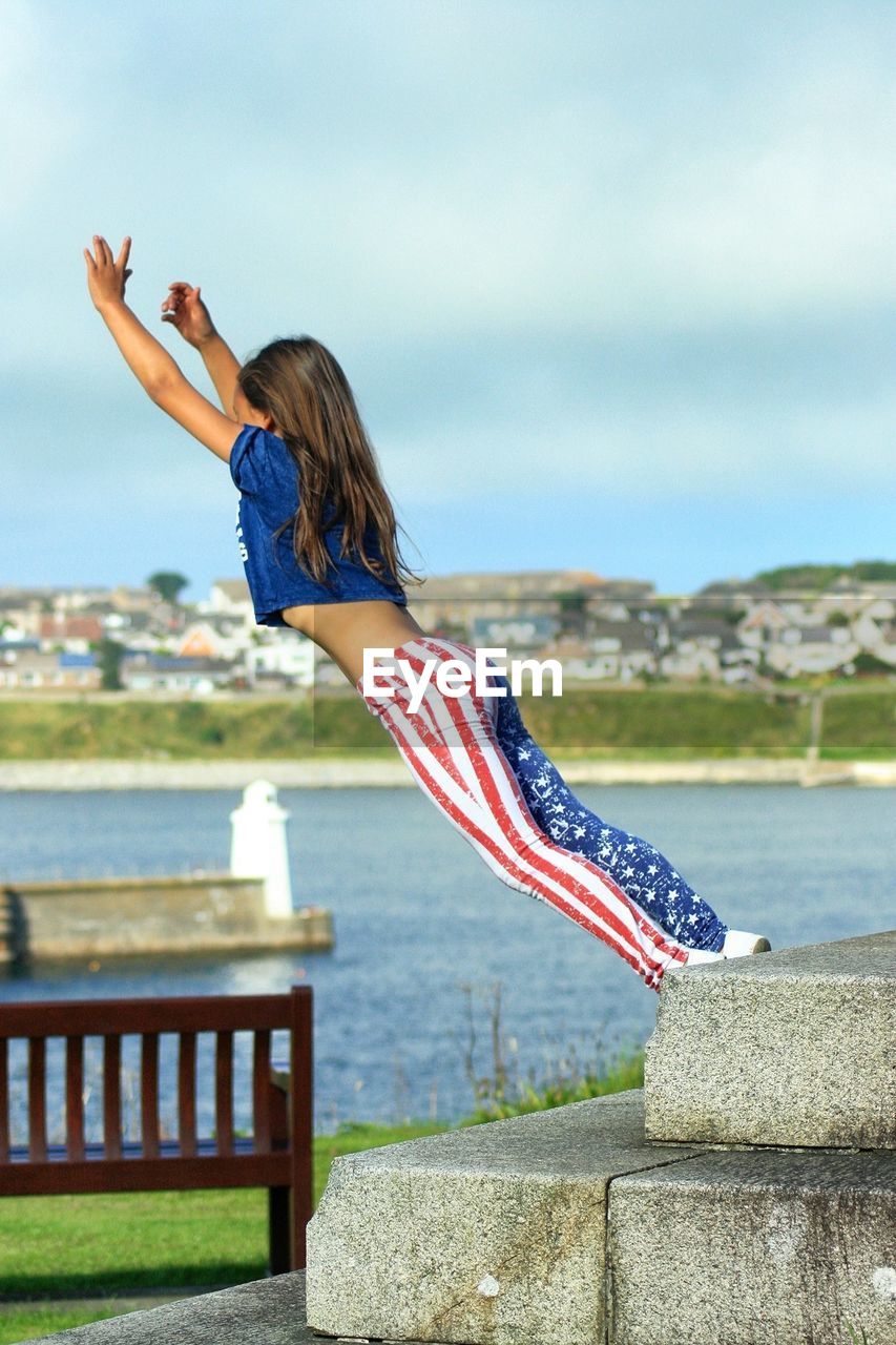 Teenage girl jumping by lake against sky