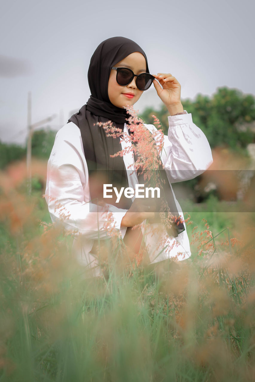 Young woman wearing sunglasses standing on field