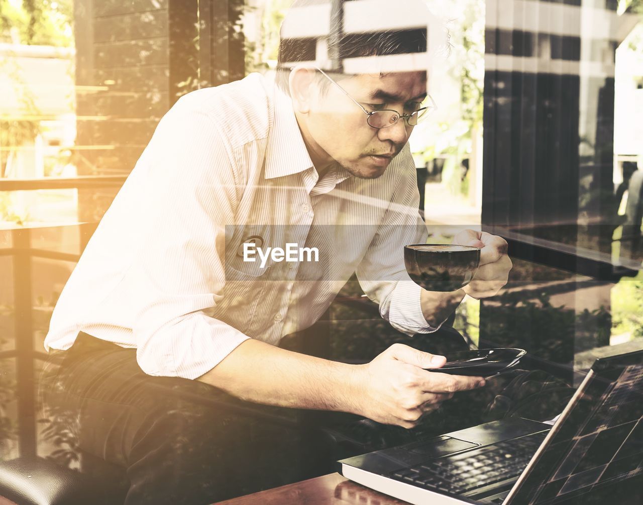 Man having coffee while using laptop at cafeteria