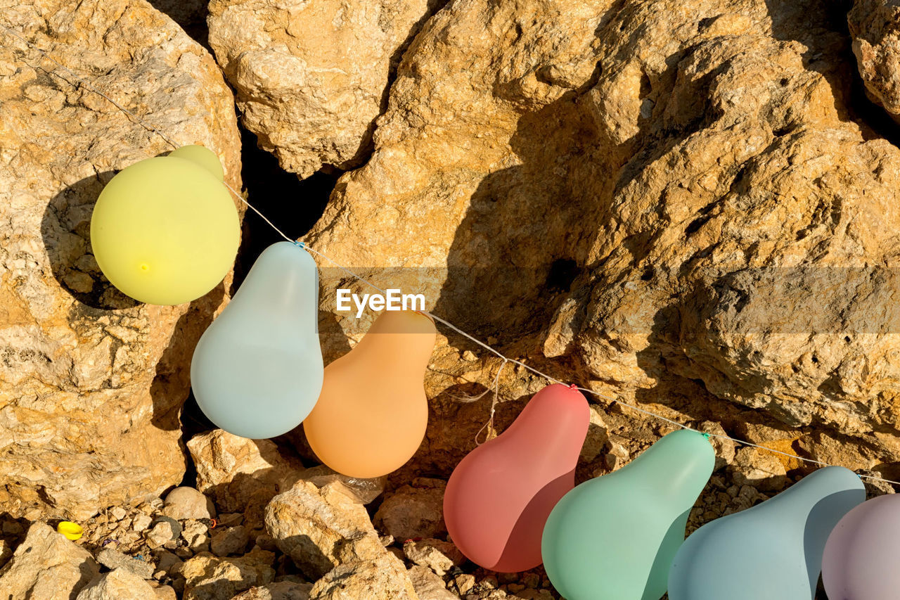 High angle view of colorful balloons tied with rope on rock during sunny day