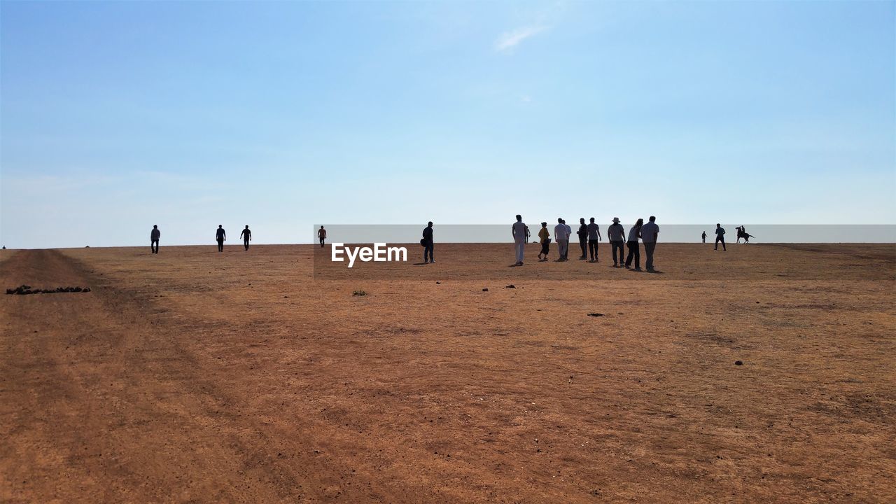 People standing on sand at desert against sky during sunny day
