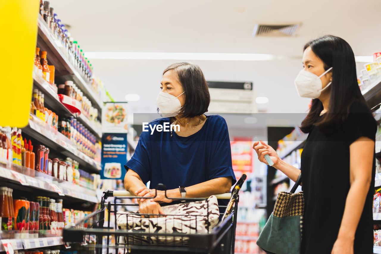 Senior woman and daughter in medical mask doing shopping in supermarket