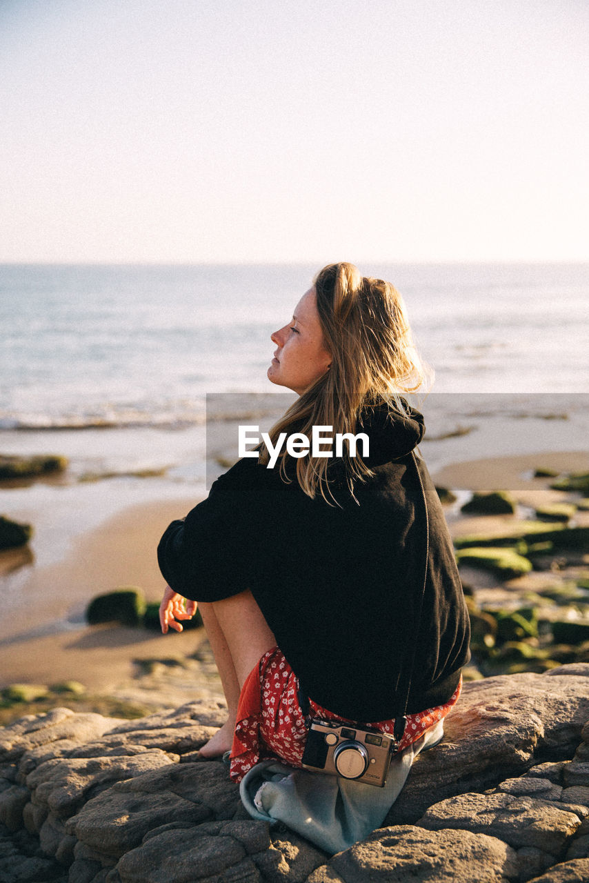 Full length of woman sitting on rock at beach