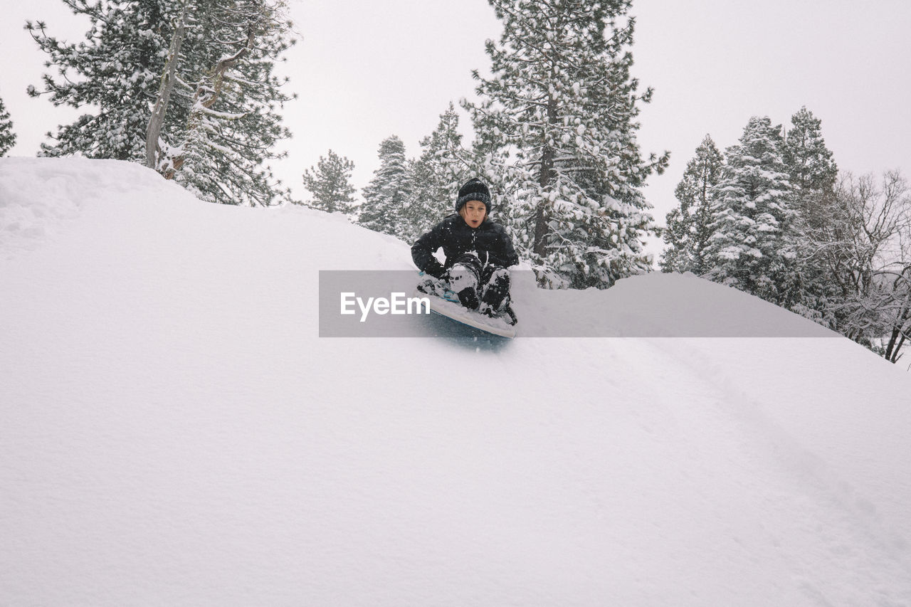 Boy starts down snowy hill on a sled.