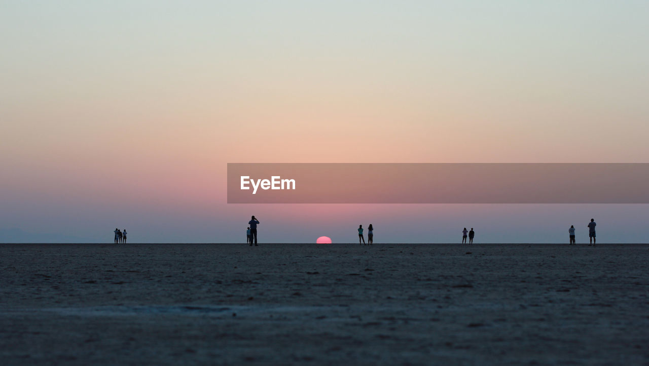 People at beach against sky during sunset