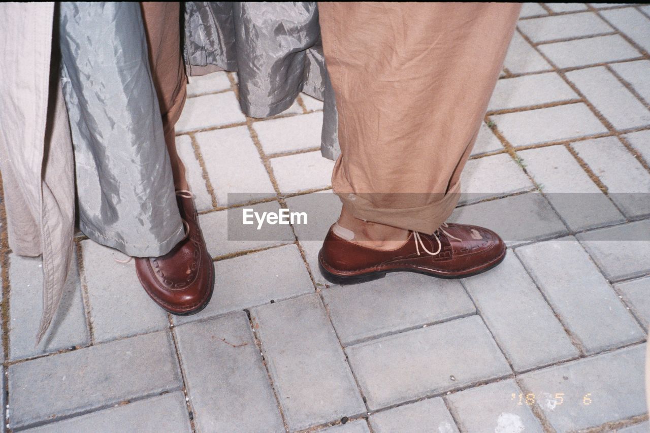 Low section of man wearing shoes while standing by curtain on paving stone