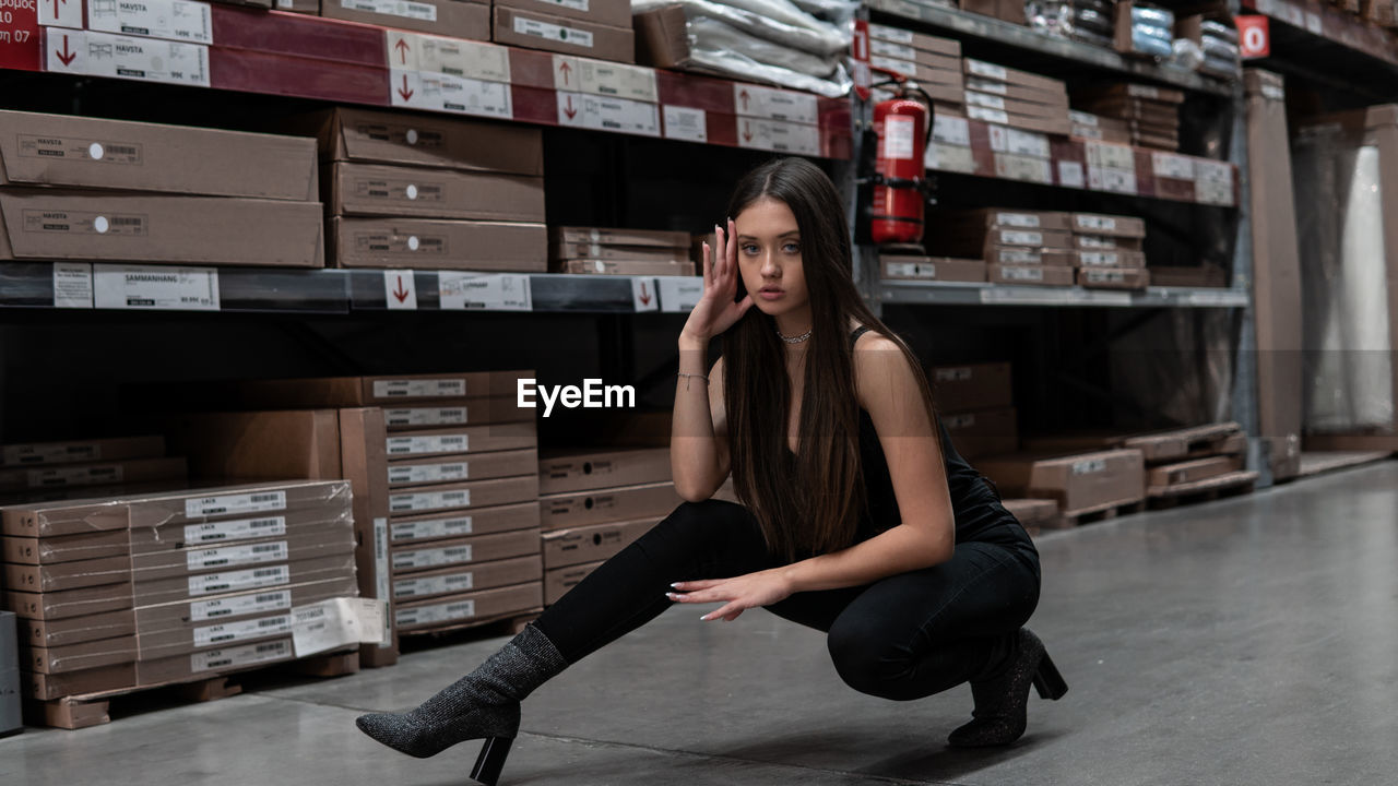 Full length portrait of young woman stretching on floor in warehouse