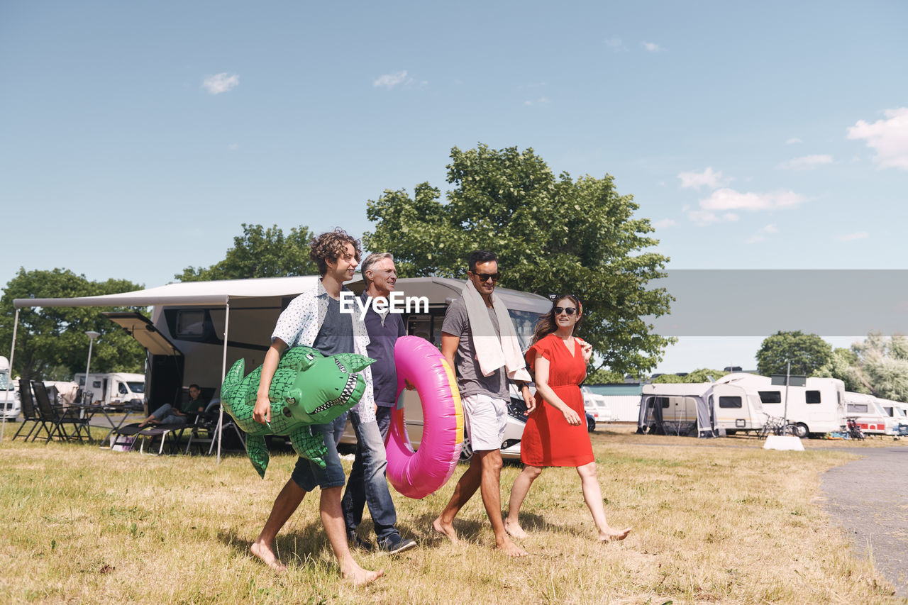 Full length of family with inflatable rings walking on grassy field against sky