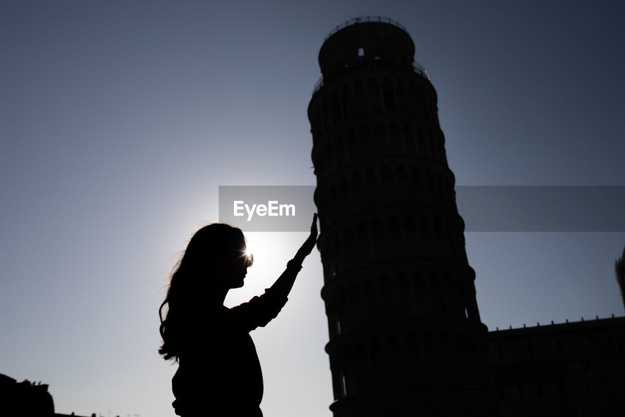 Optical illusion of silhouette woman holding leaning tower of pisa against clear sky