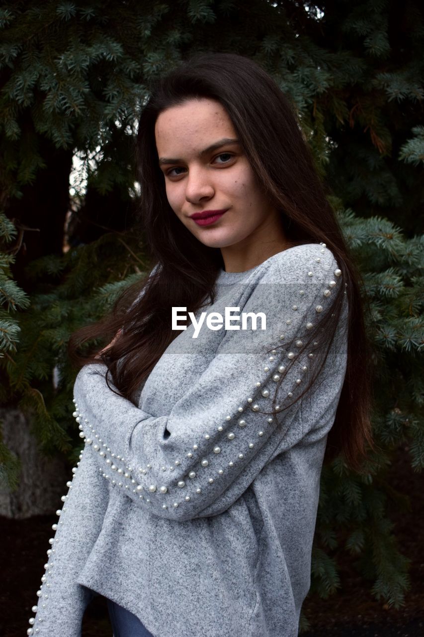 PORTRAIT OF BEAUTIFUL YOUNG WOMAN STANDING AGAINST TREES