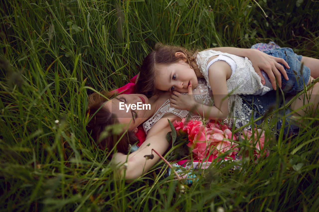 Mother and daughter lie on a green field in summer and relax in the sun