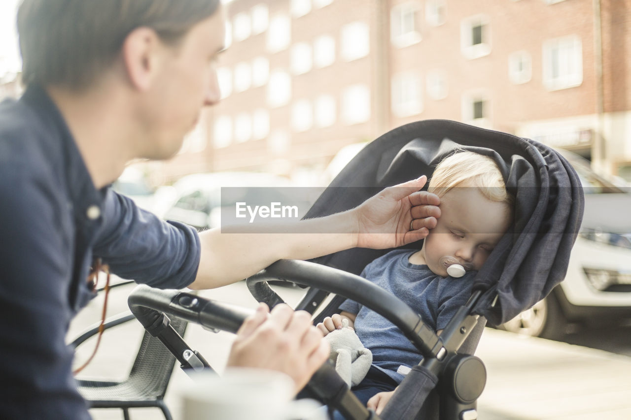 Father looking at baby sleeping on stroller in city