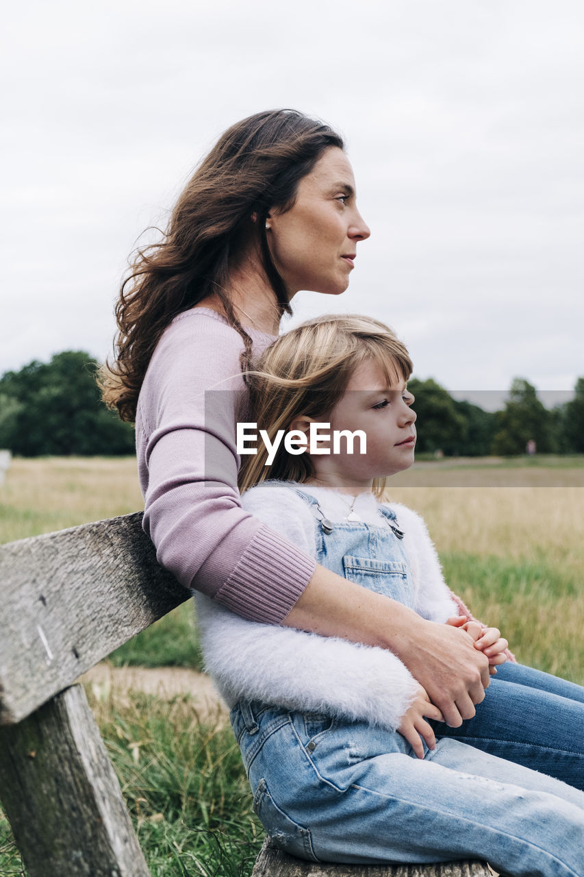 Woman with arms around daughters sitting on bench