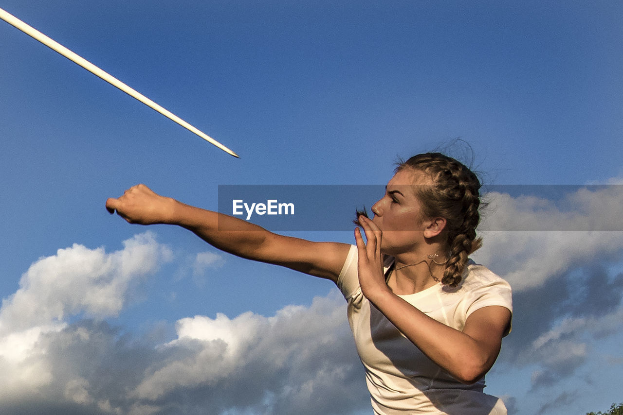 Low angle view of athlete throwing javelin against blue sky