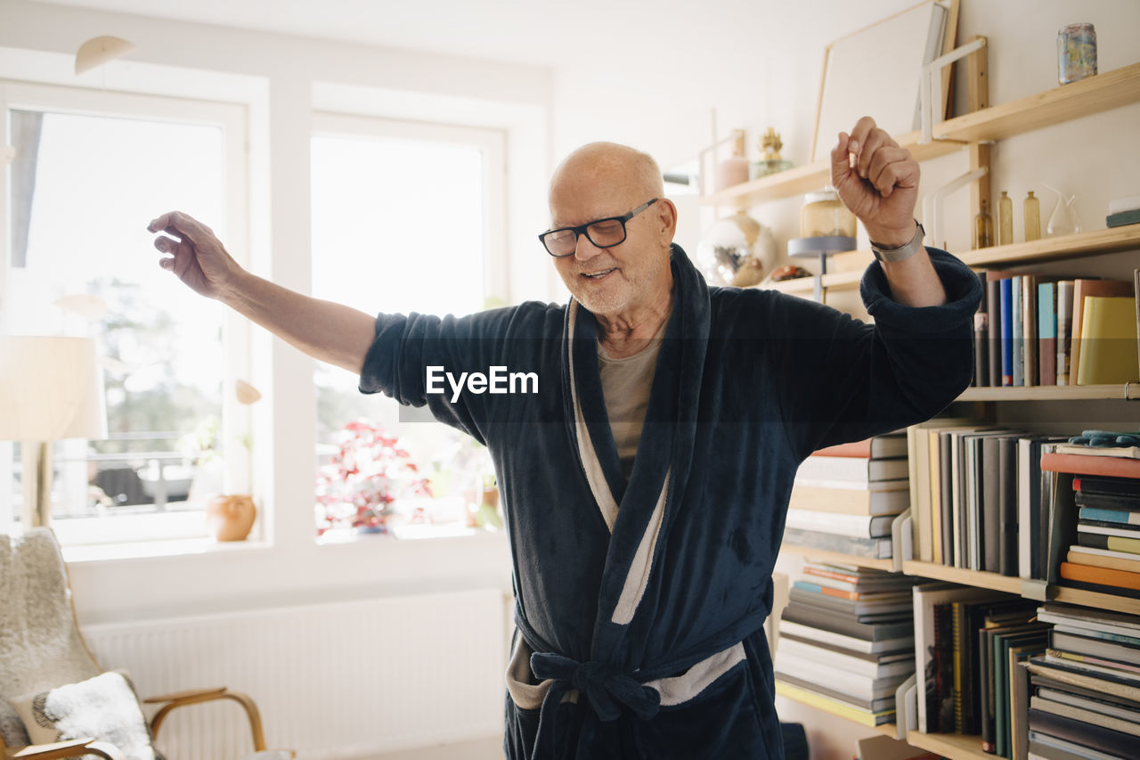 Senior man in bathrobe dancing in living room at home