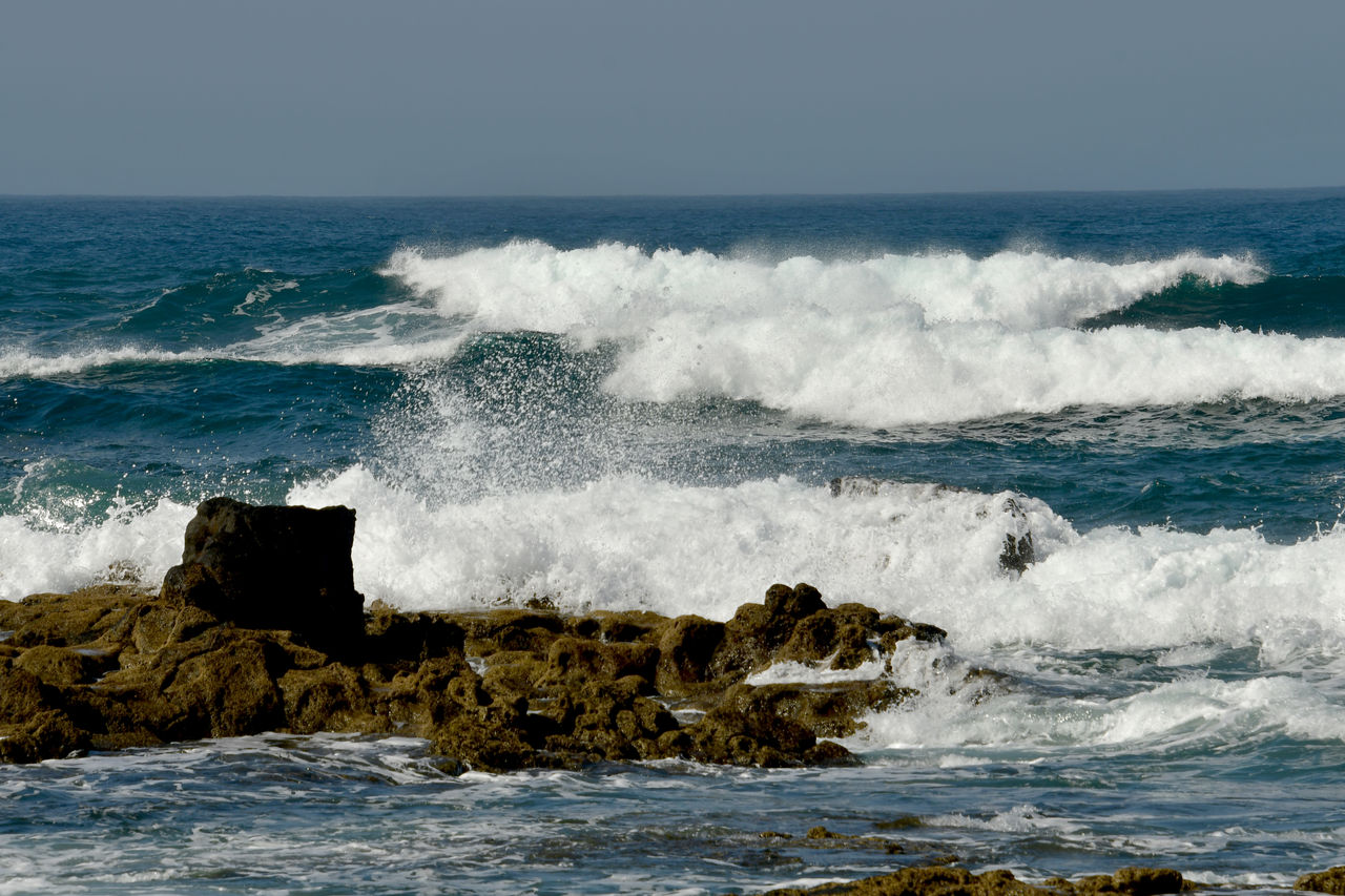 Waves splashing on rocks at sea against sky