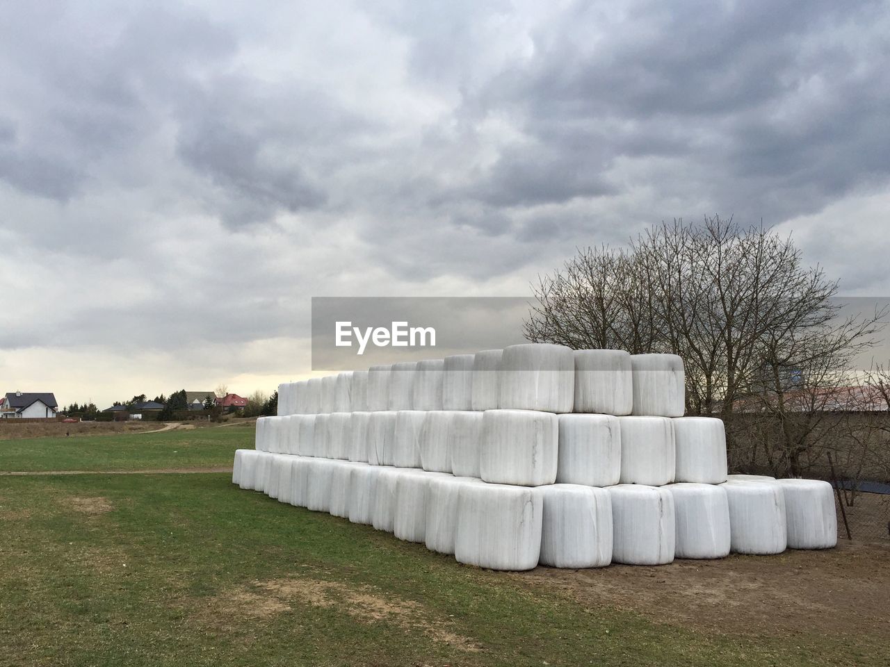 Stack of white hay bales on field against cloudy sky