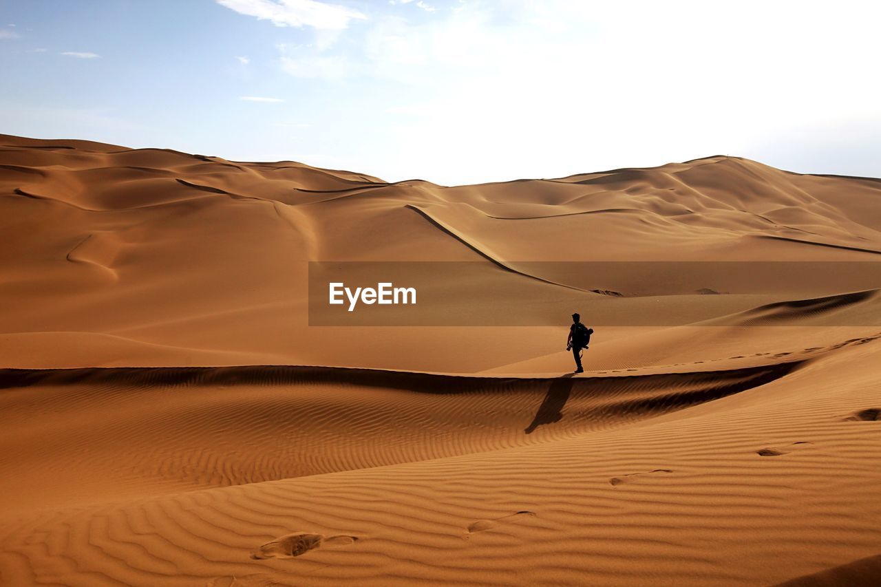 Man standing on sand dunes at desert against sky