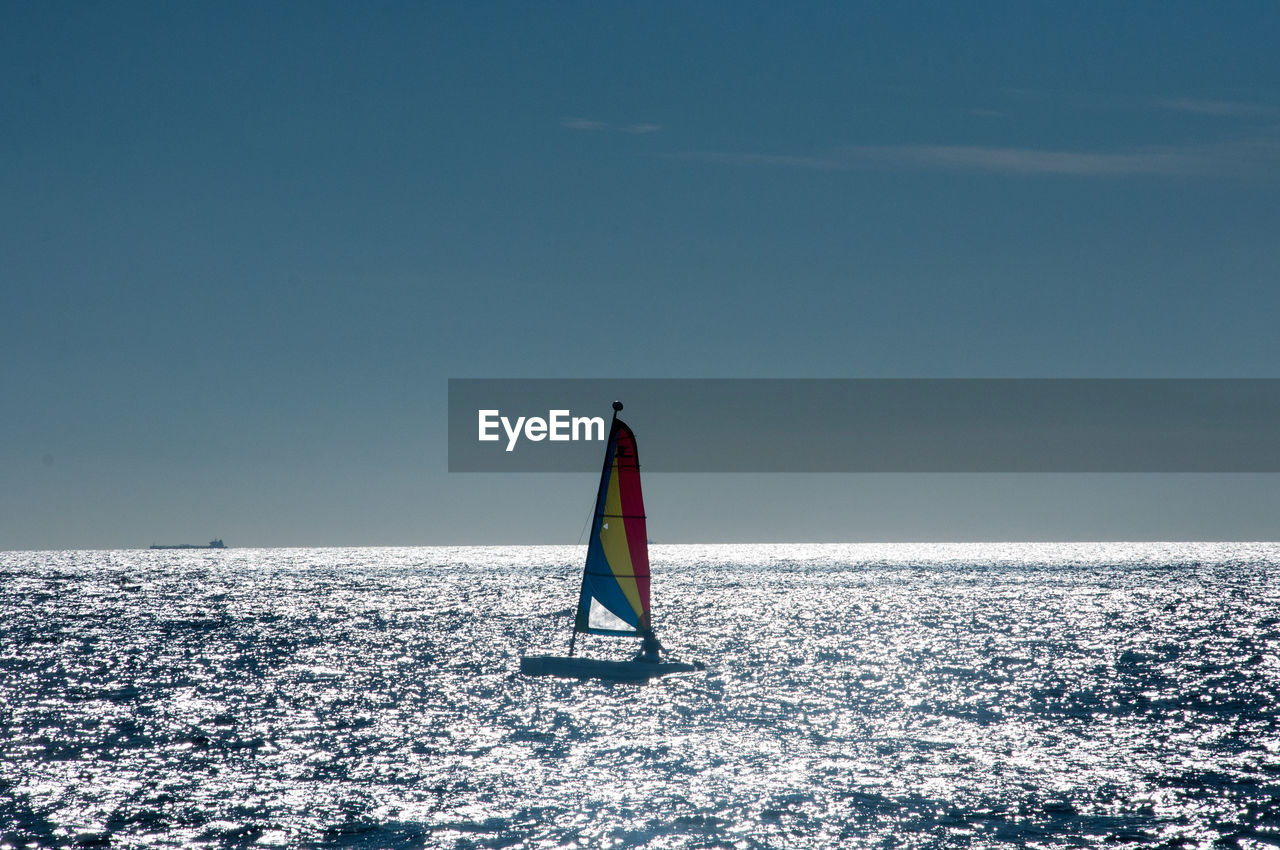 sailing, water, sea, ocean, sky, nature, vehicle, boat, horizon over water, beauty in nature, sailboat, sports, copy space, horizon, scenics - nature, blue, windsurfing, nautical vessel, ship, wave, wind wave, travel, tranquility, day, clear sky, adventure, outdoors, wind, tranquil scene, environment, sunlight, transportation, holiday, leisure activity, water sports, vacation, one person, motion, travel destinations, cold temperature, sunny, trip, watercraft, non-urban scene
