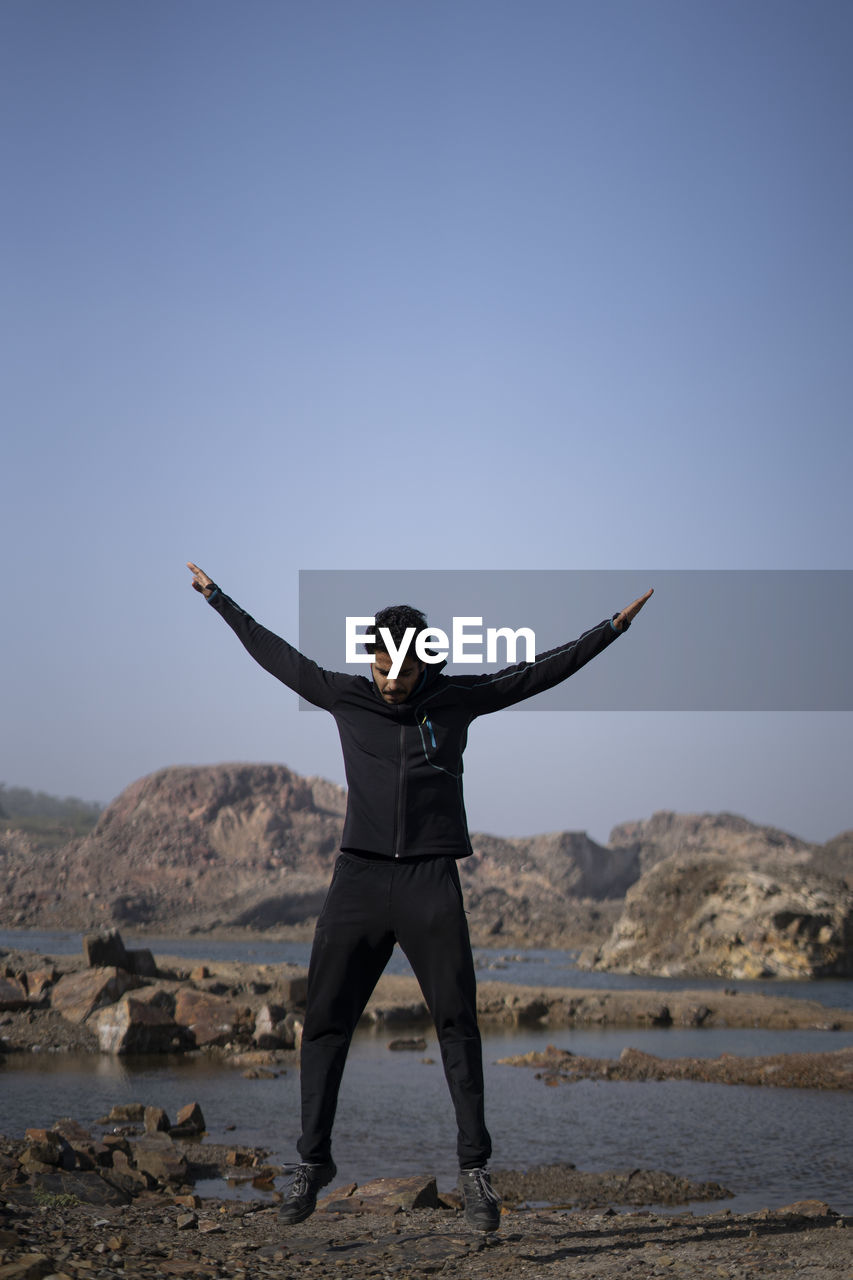 MAN STANDING ON BEACH AGAINST SKY