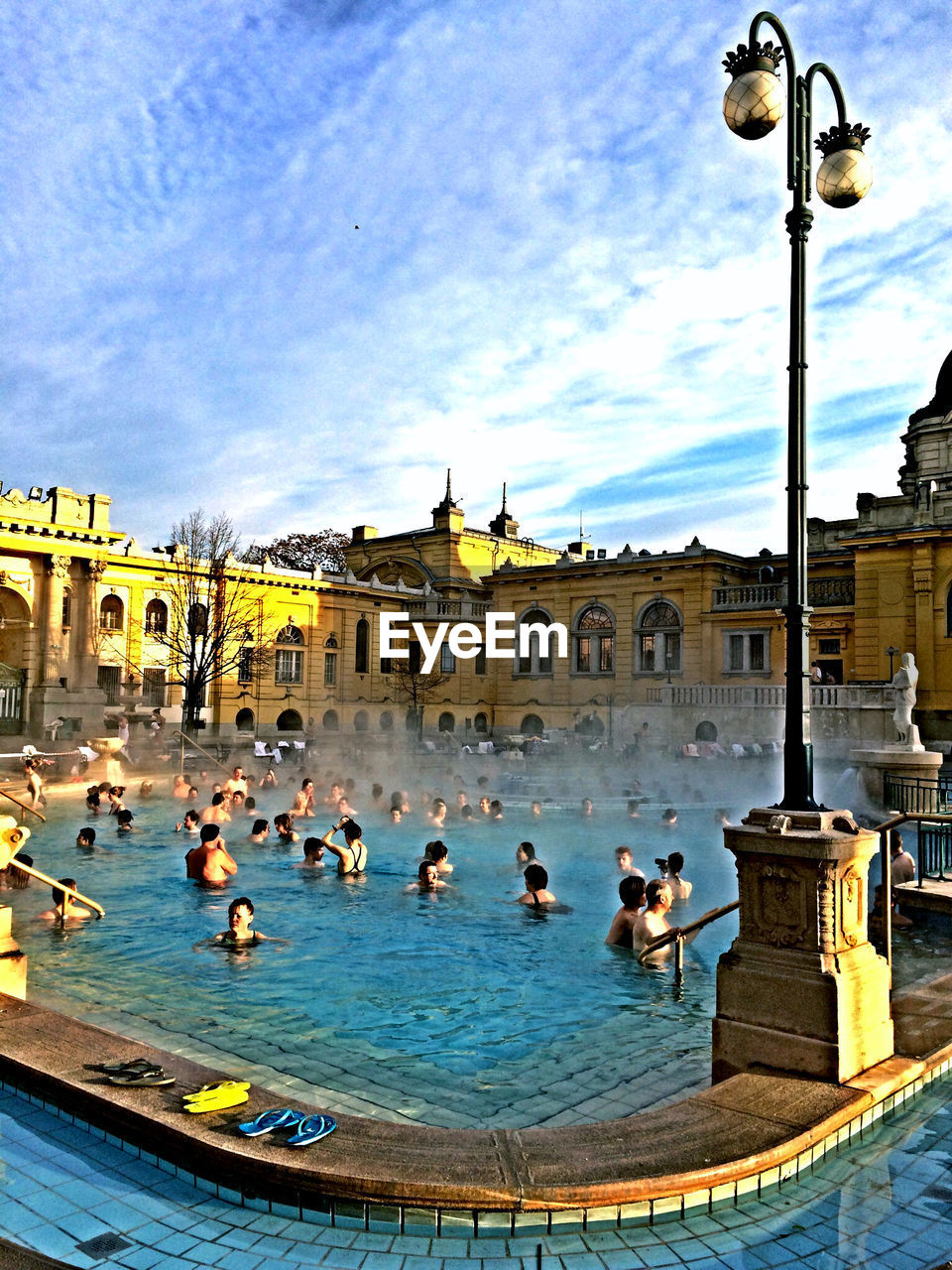 High angle view of people enjoying in swimming pool by hotel against sky