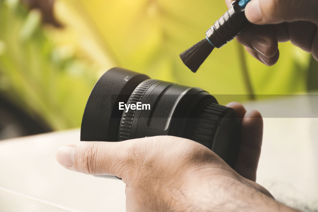 Human hand cleaning dust on camera lens with pen brush cleaner