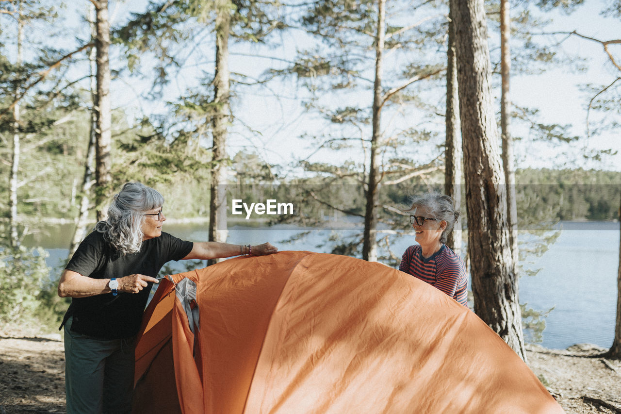 Two senior women setting up tent at campsite at lakeshore