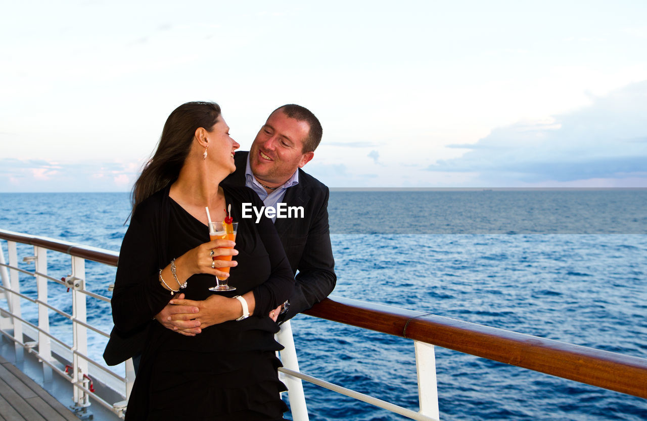 Loving mature couple standing in ship on sea during sunset