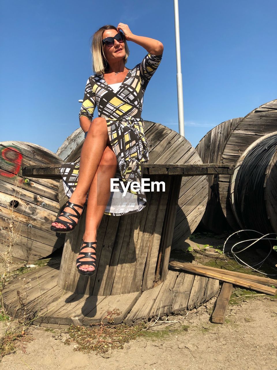 Woman wearing sunglasses while sitting on wooden spool