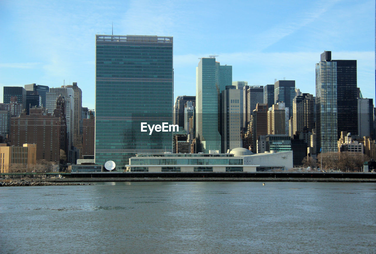 Modern buildings by river against sky in city