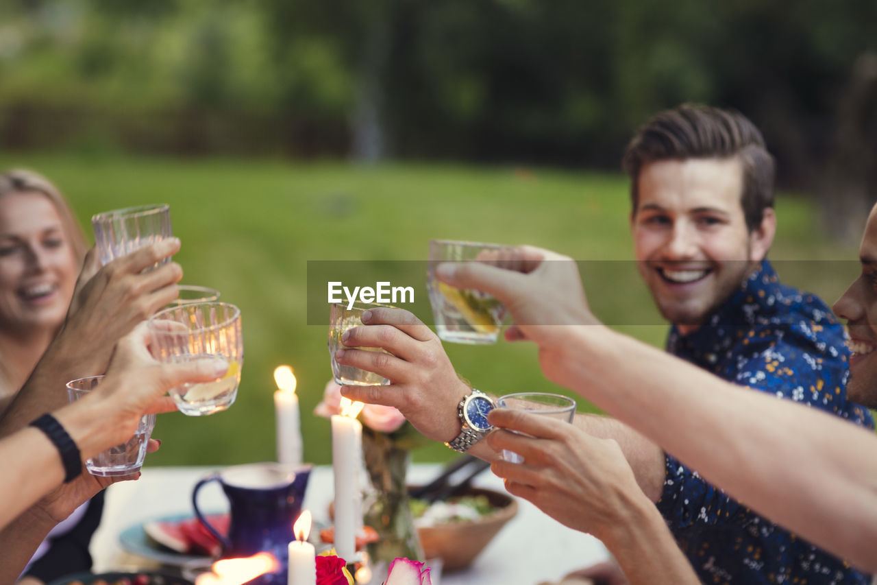 Happy friends toasting glasses while enjoying meal at garden party