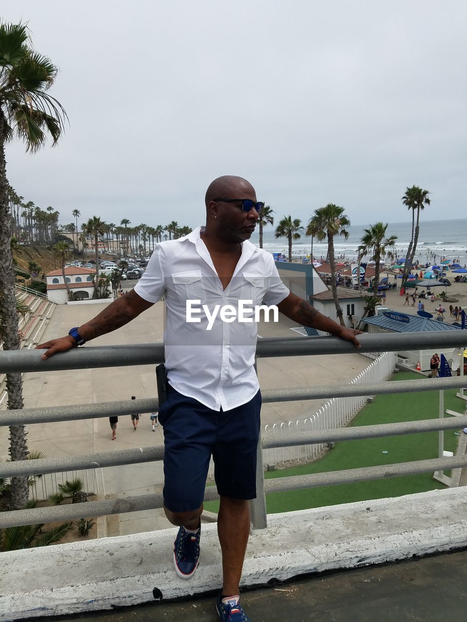 Mature man wearing sunglasses standing by railing against beach