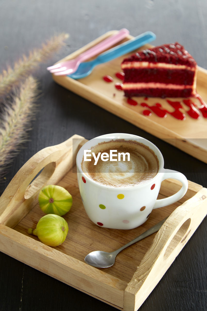 Close-up of coffee cup and figs in serving tray with red velvet cheesecake slice in background