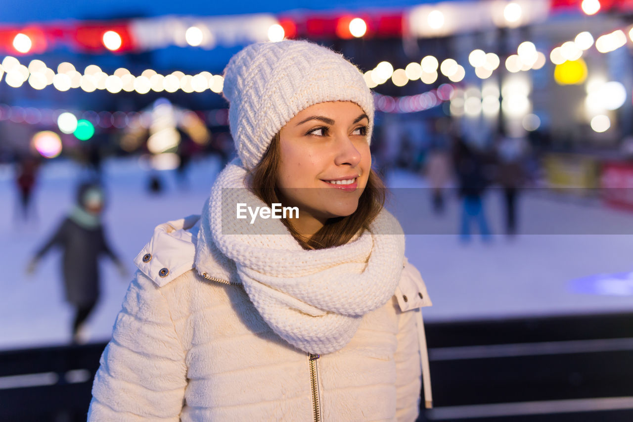 PORTRAIT OF SMILING YOUNG WOMAN STANDING IN ILLUMINATED DURING WINTER