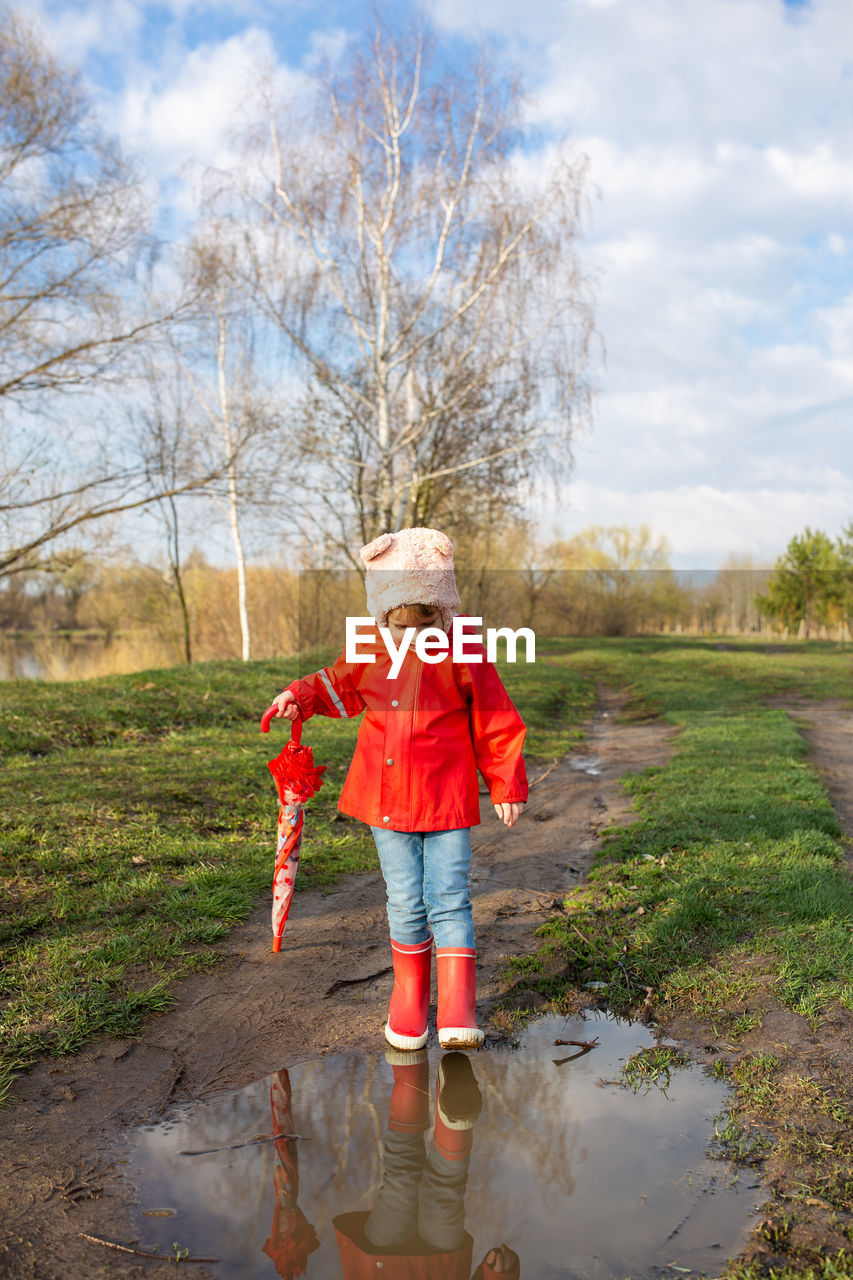 Child plays with umbrella after the rain in red rubber boots and a raincoat.