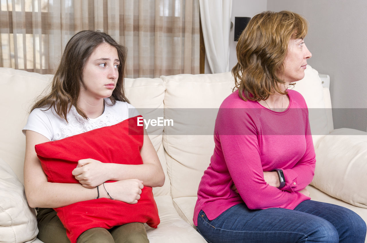 Daughter holding cushion looking at angry mother on sofa at home