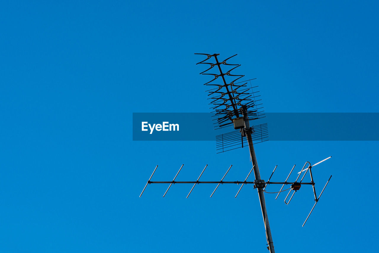 technology, blue, sky, television antenna, antenna, line, communication, clear sky, electronic device, electricity, nature, no people, low angle view, wind, telecommunications equipment, mast, overhead power line, day, telecommunications engineering, outdoors, power generation, television aerial, copy space, wireless technology, broadcasting, sunny