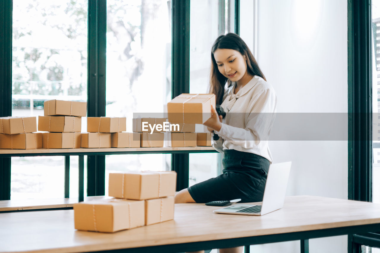 Young businesswoman working while sitting by packages at office