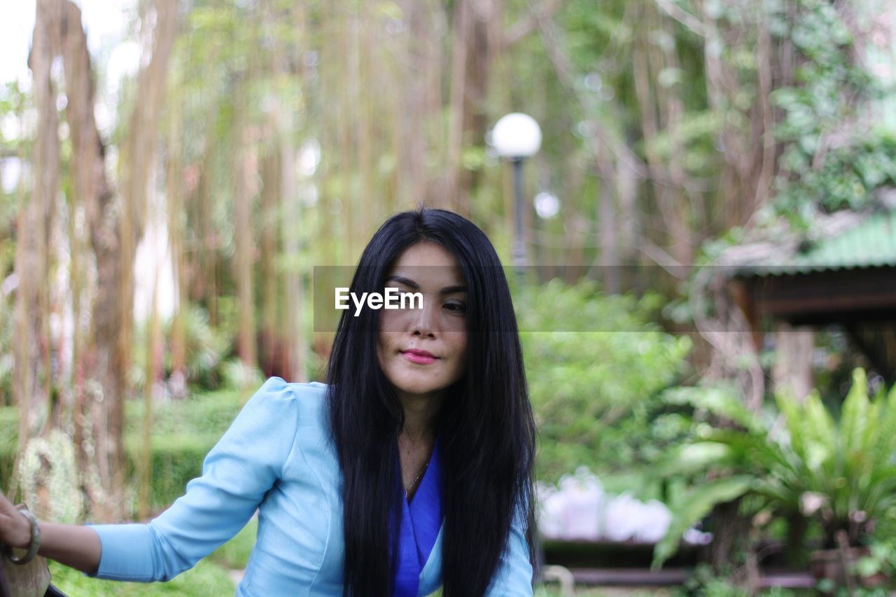 Thoughtful beautiful woman standing against trees in forest