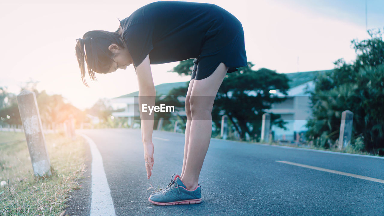 Side view of woman exercising while standing on road