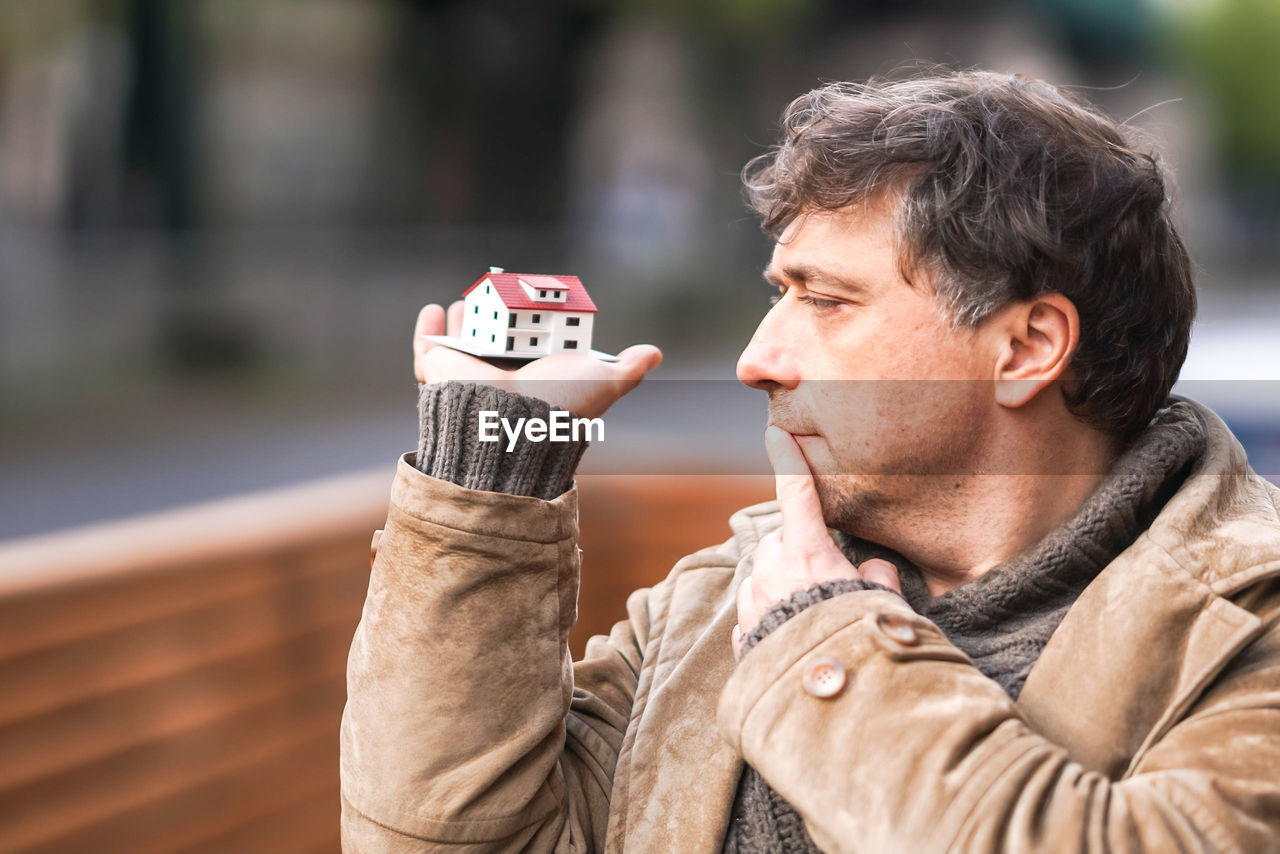 Close-up of man holding model house in city