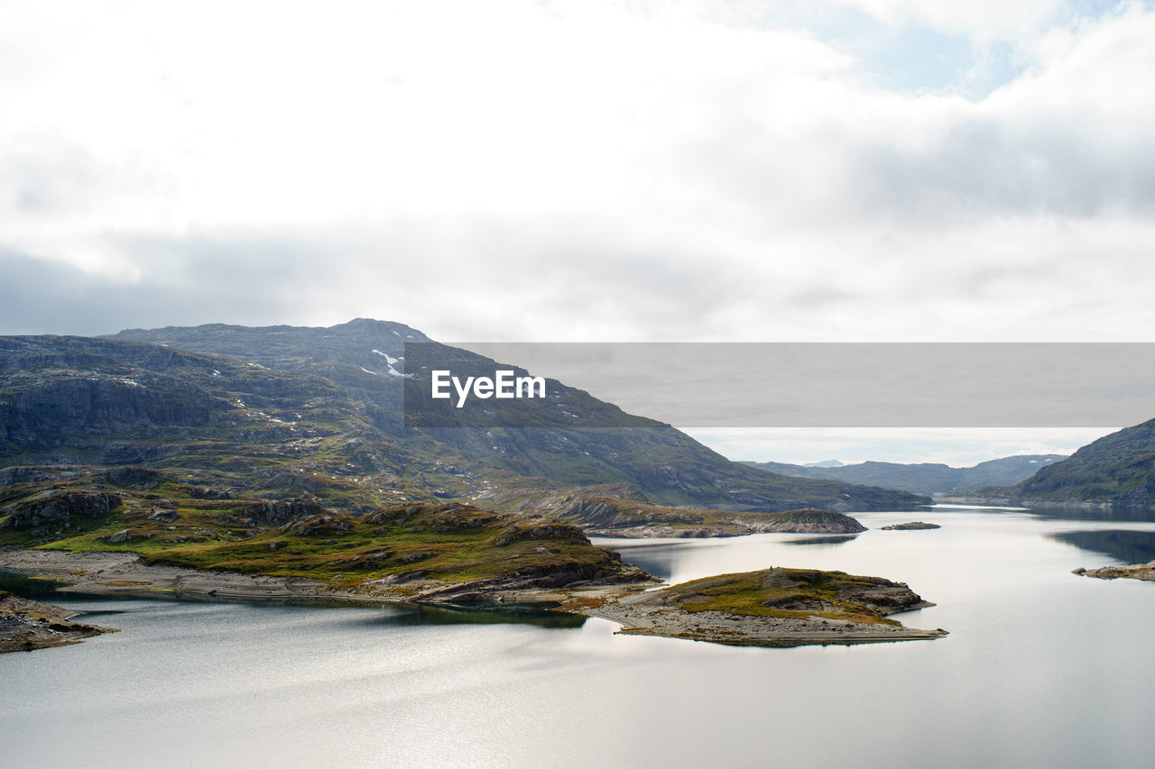 Scenic view of calm lake and mountains against cloudy sky