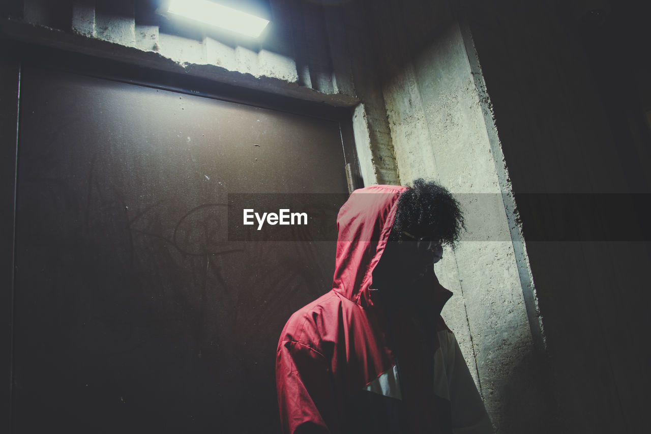 Man wearing hood while standing against wall at night