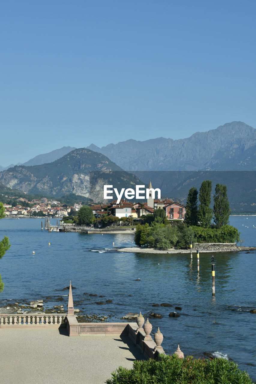 HOUSES BY LAKE AND MOUNTAINS AGAINST CLEAR BLUE SKY