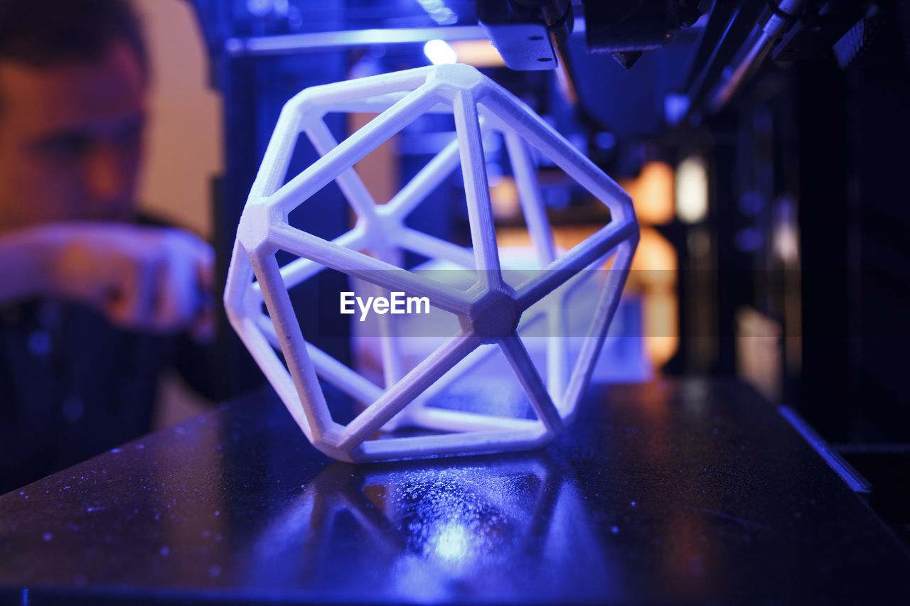 3d geometric figure on the platform of a 3d printer with a man in the background